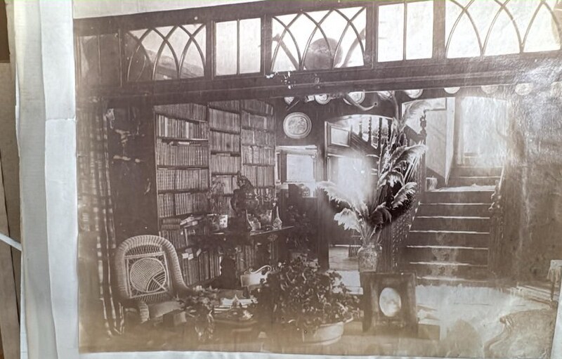 A Victorian photograph inside Island House: a room lined with bookcases and filled with plants, beneath a glazed screen of pointed Gothic tracery.