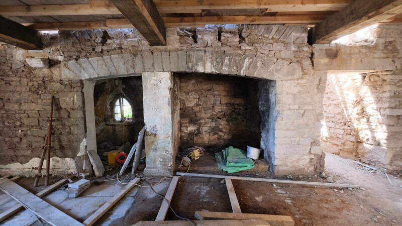 The great inglenook of Island House today: a very wide fireplace opening spanned by a massive cambered stone bressumer, with a deep open hearth beneath it and a smaller arched recess alongside holding a little cusped window.