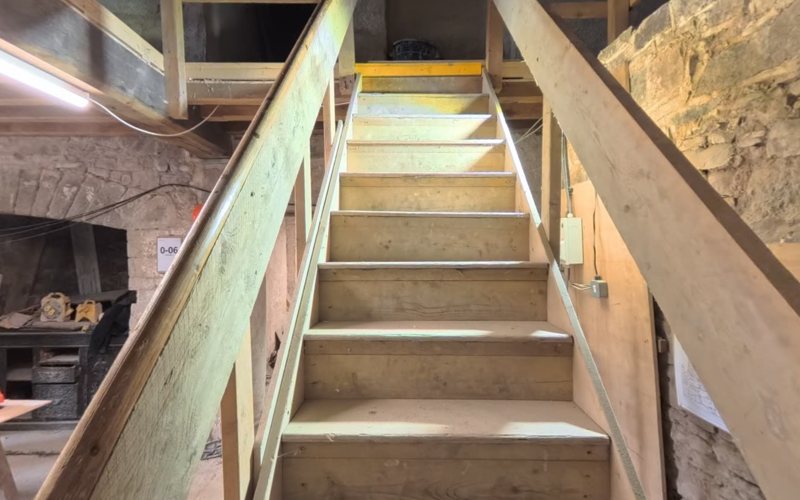 The stair of Island House today: a plain timber flight rising within a stone shaft, boarded for protection during the restoration.