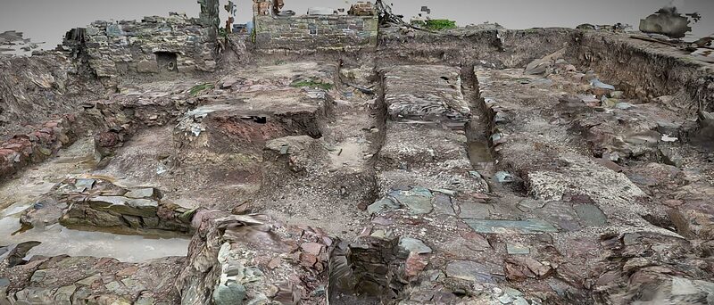 The excavated quay beside Island House: cut trenches and exposed stone footings, the house and castle wall behind.